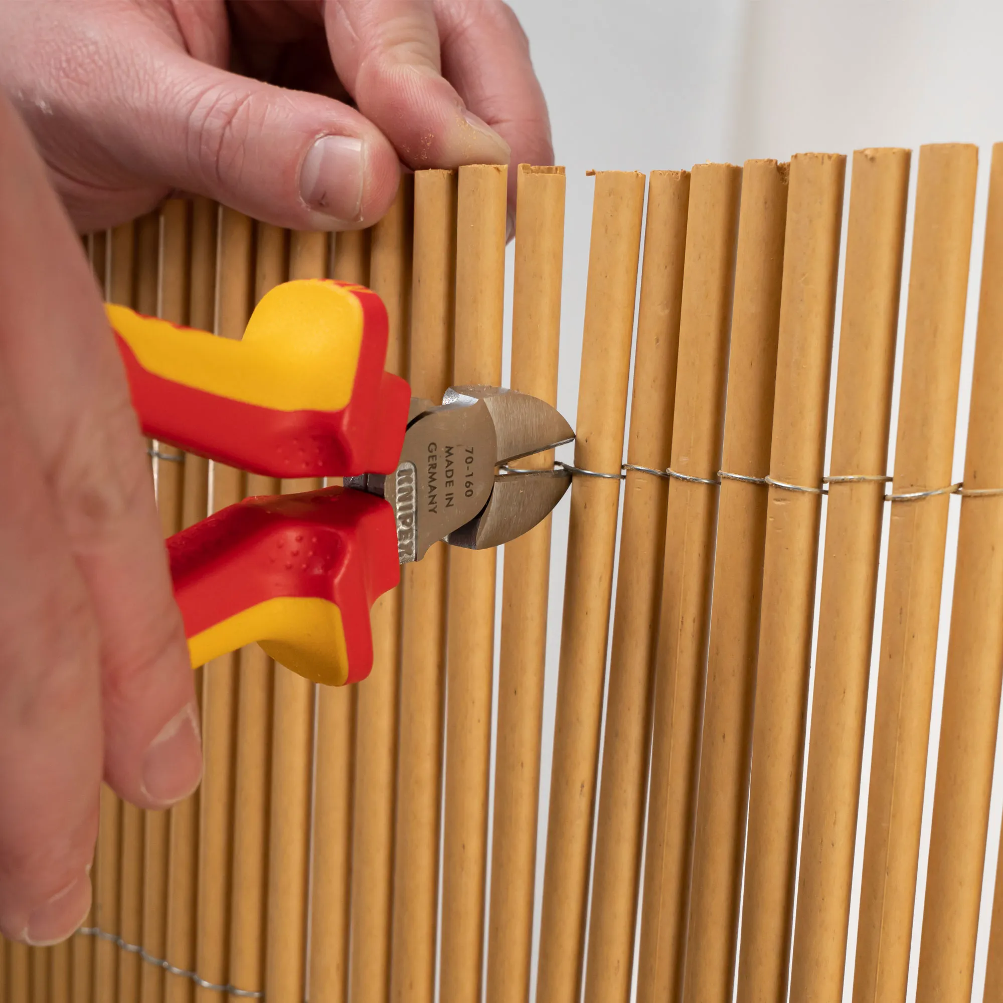 Mano che tiene una pinza, taglia un filo su una stuoia di bambù