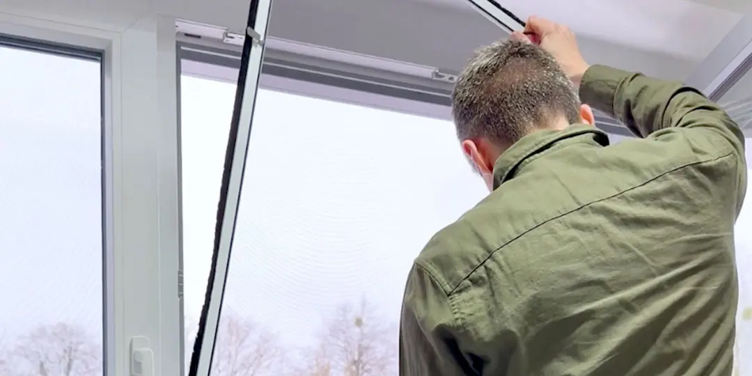 Mann bringt vormontierten Insektenschutz ans Fenster an.