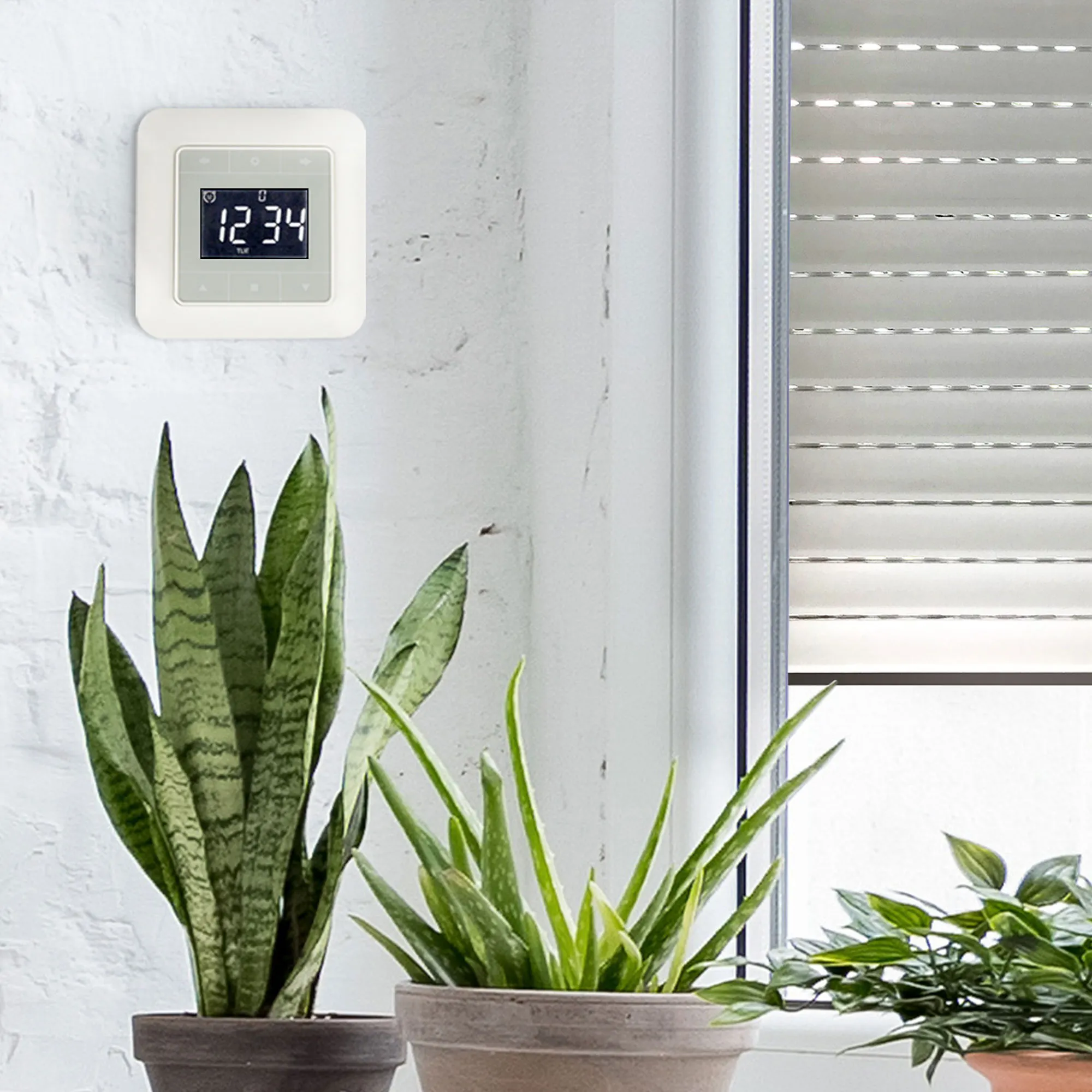 Timer con display touch montato a parete accanto a piante e una finestra con persiana