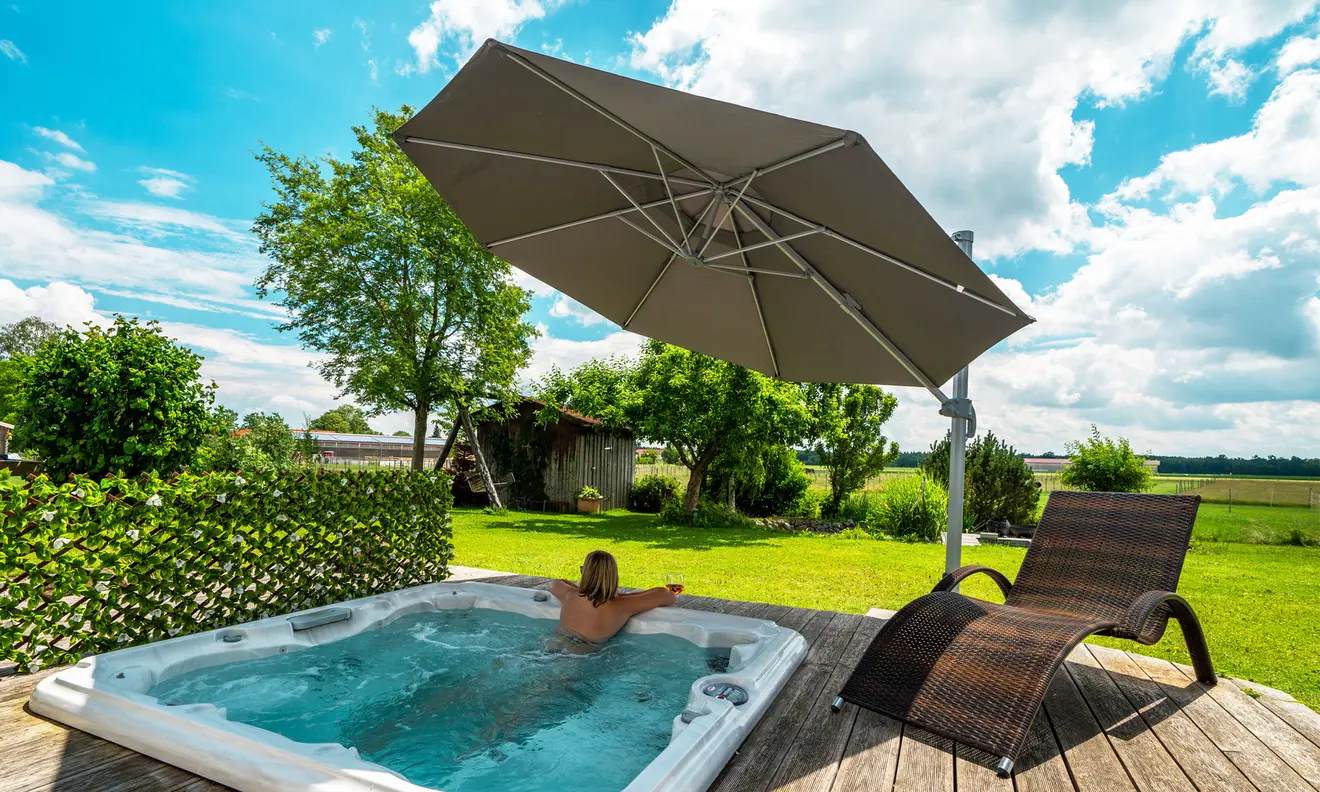 Ampelschirm über einem Whirlpool im Garten, daneben eine Liege auf Holzterrasse