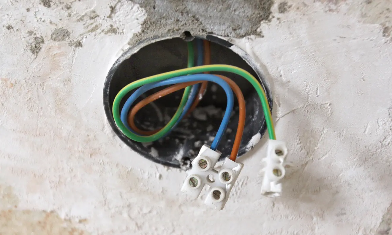 Unterputzdose mit sichtbaren Kabeln und Anschlussklemmen in einer Wandöffnung