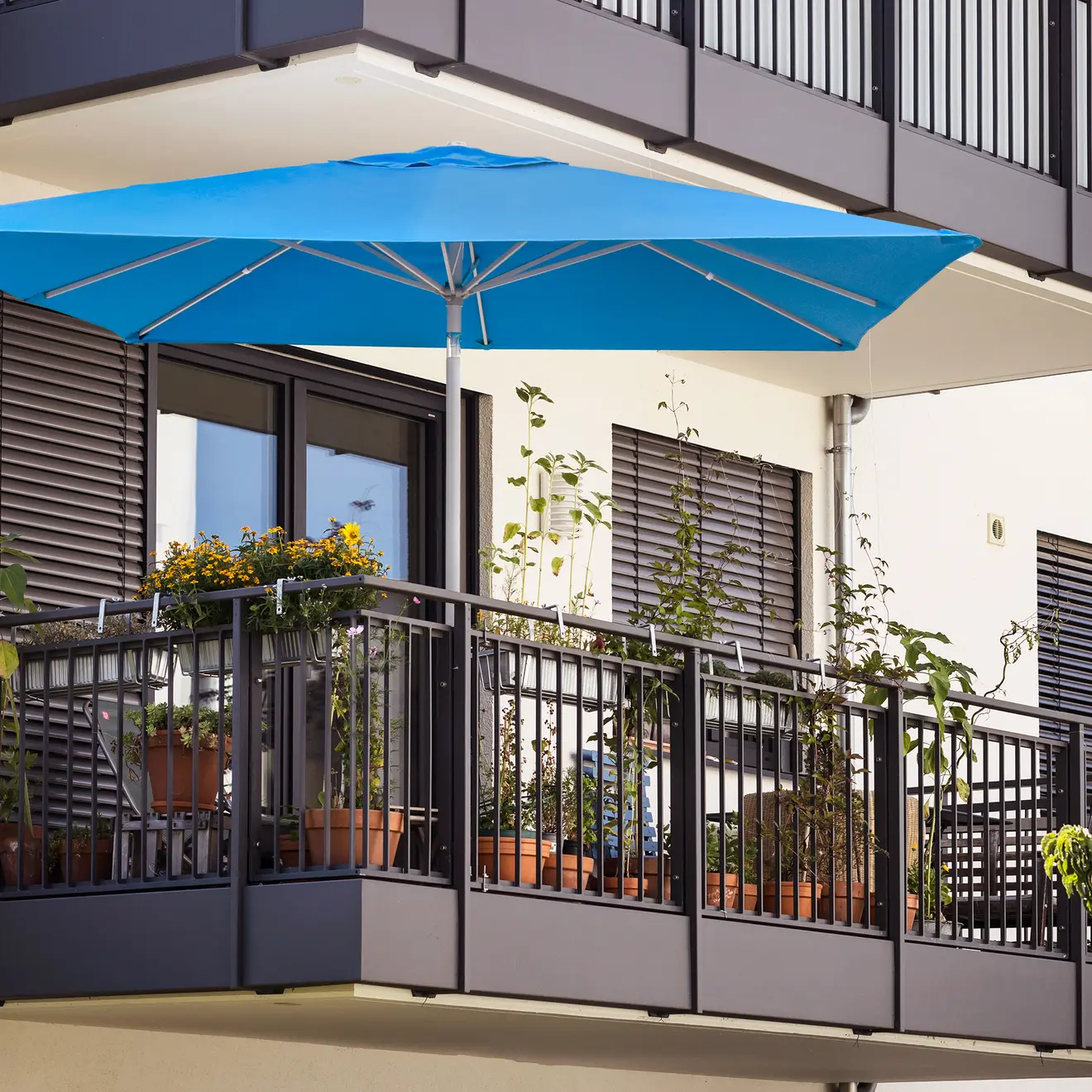 Blauer Sonnenschirm über Balkon mit Pflanzen und moderner Hausfassade