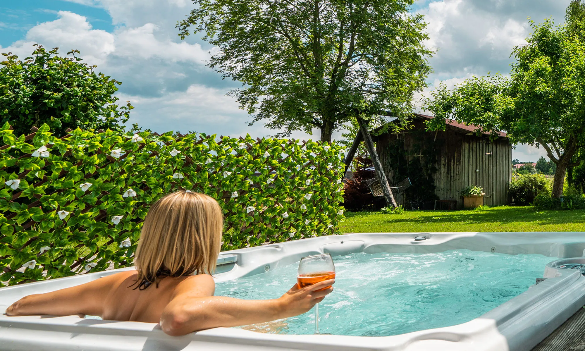 Persona rilassata in una vasca idromassaggio, parete di piante artificiali sullo sfondo, ambiente da giardino