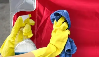 Person reinigt Faltpavillon mit Sprühflasche und Tuch