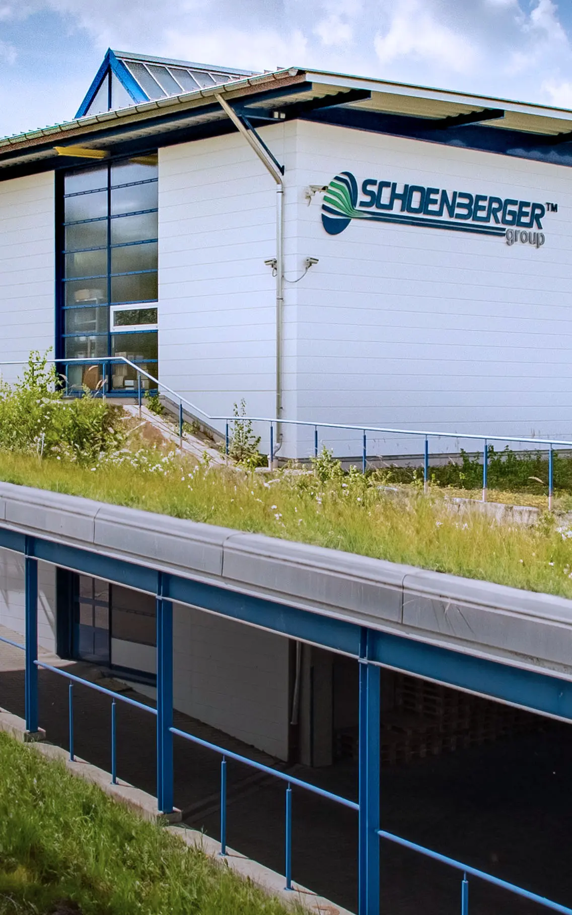 Industriegebäude mit Glasfassade und begrüntem Dach, Treppe führt zum Eingang