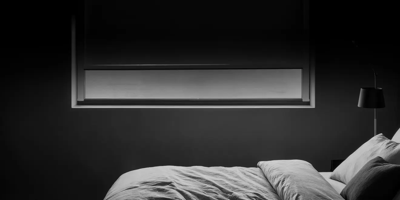 Schlafzimmer mit Fenster, heruntergelassenem Rollo und Bett im Vordergrund