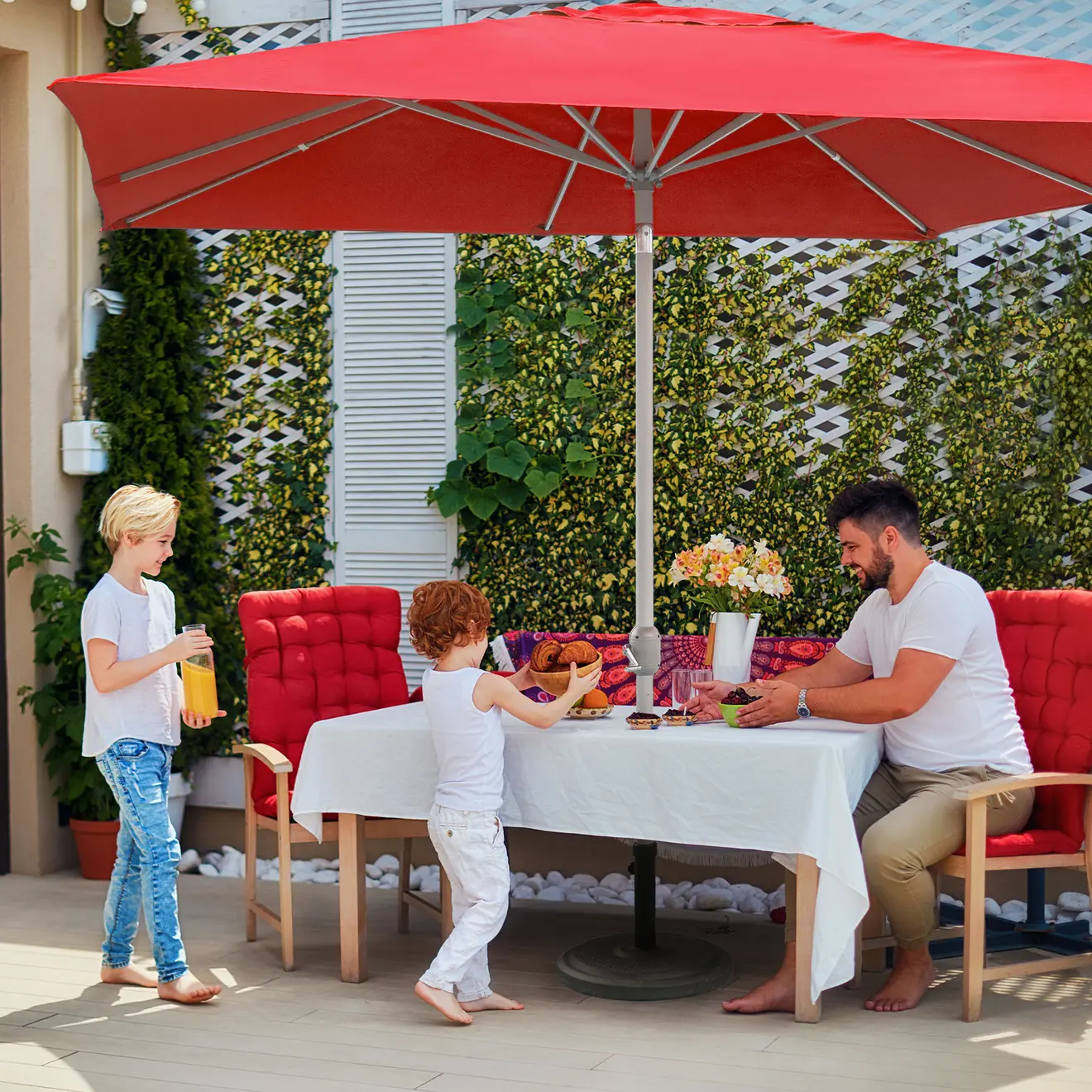 Familie sitzt am Tisch unter Sonnenschirm auf Terrasse im Garten