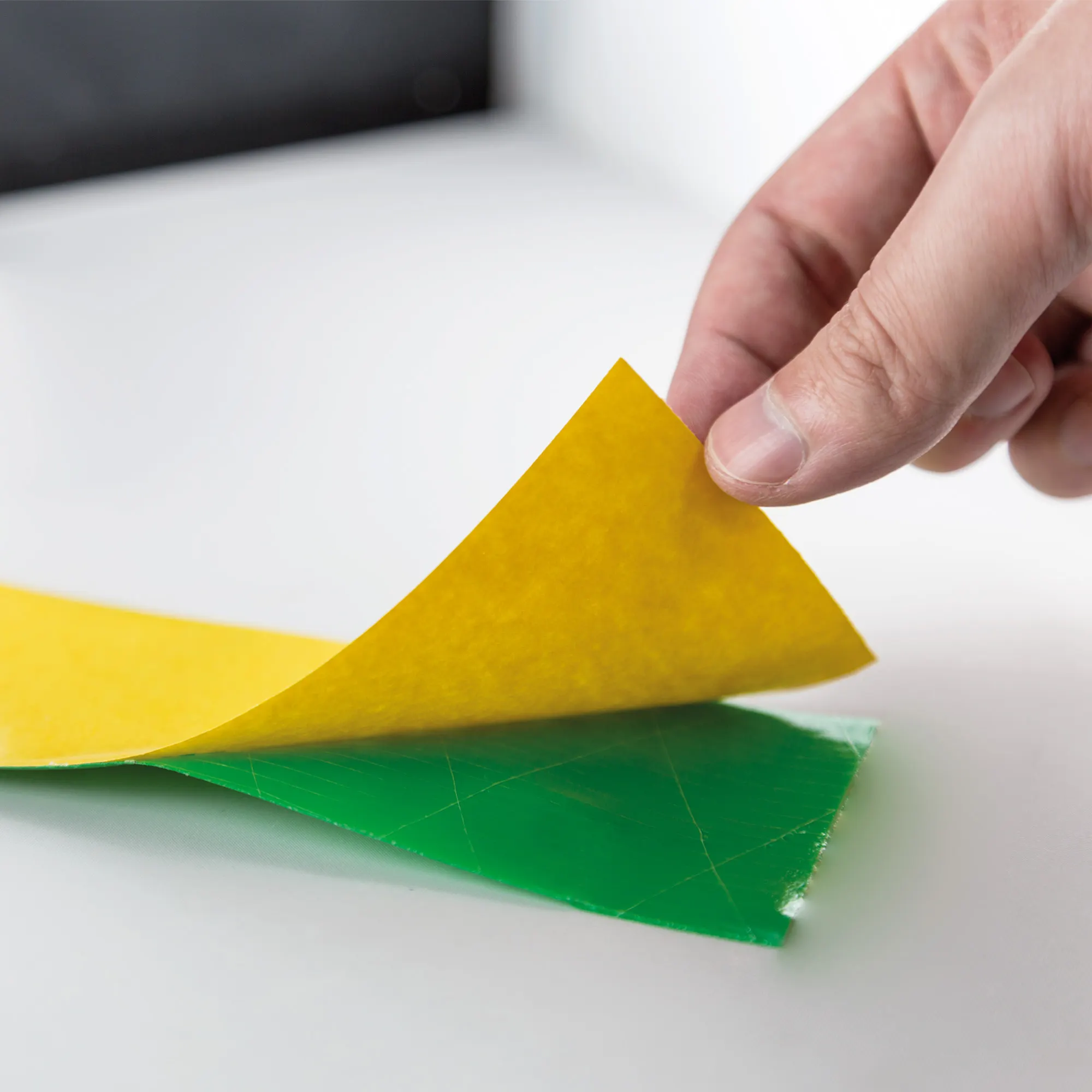 Mano che rimuove la pellicola protettiva da un nastro adesivo, mostra strati e funzione del prodotto