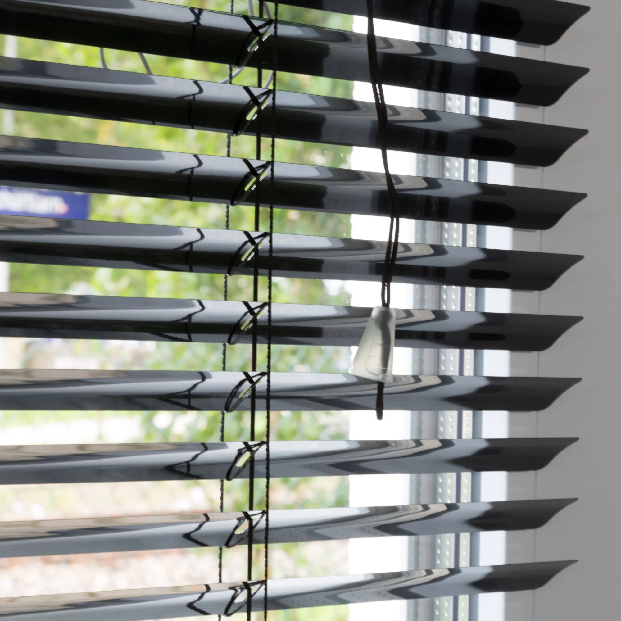 Persiana in alluminio con lamelle e cordino davanti a una finestra