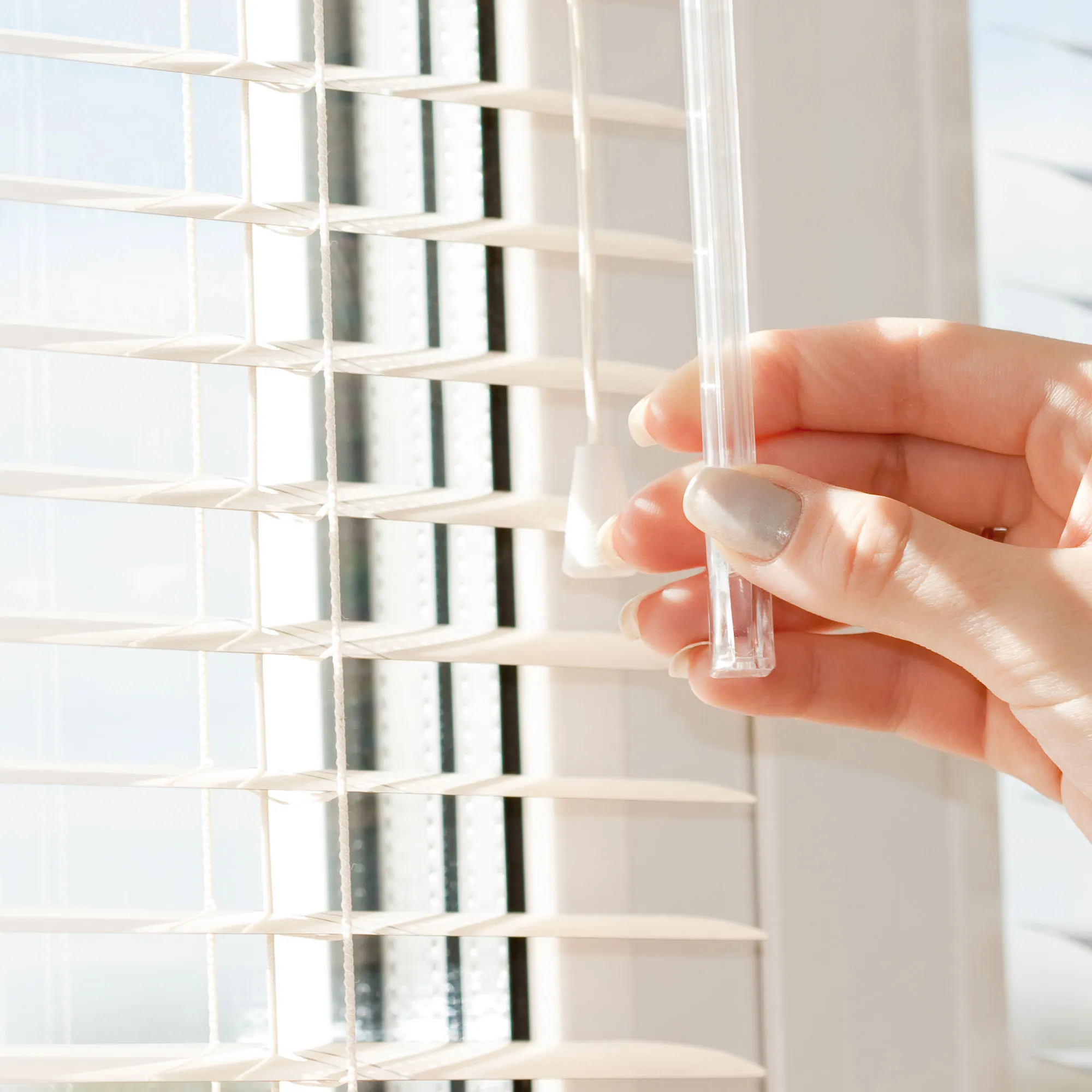 Una mano ruota un bastone di acrilico per veneziane in alluminio davanti a una finestra