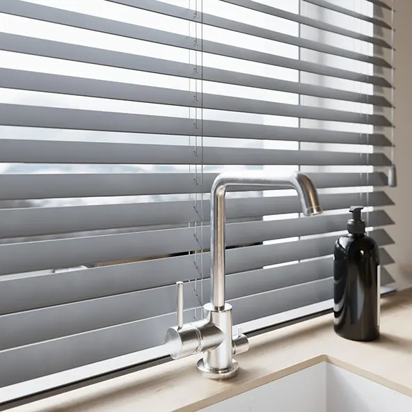 Jalousien vor einem Fenster mit Wasserhahn und Seifenspender im Vordergrund