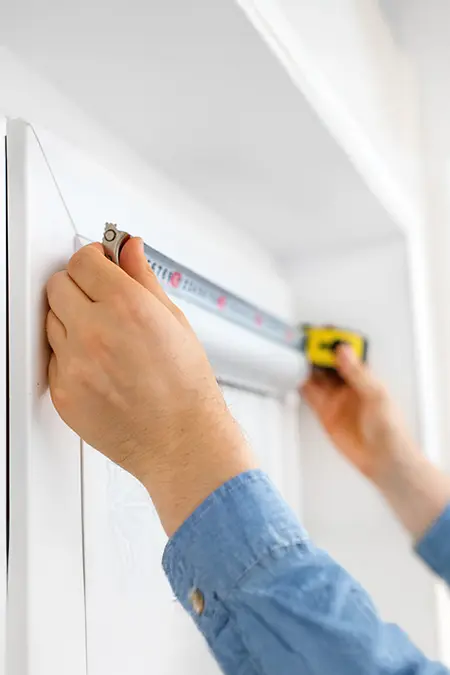 Person misst Fensterrahmen mit einem Maßband