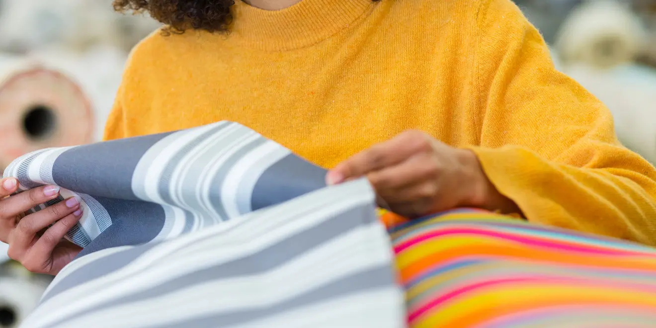 Persona sceglie tessuti per tende da sole, motivi a righe e rotoli colorati in mano
