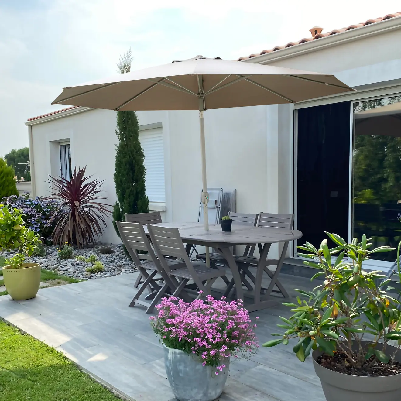 Sonnenschirm über Gartentisch auf Terrasse vor Haus mit Pflanzen