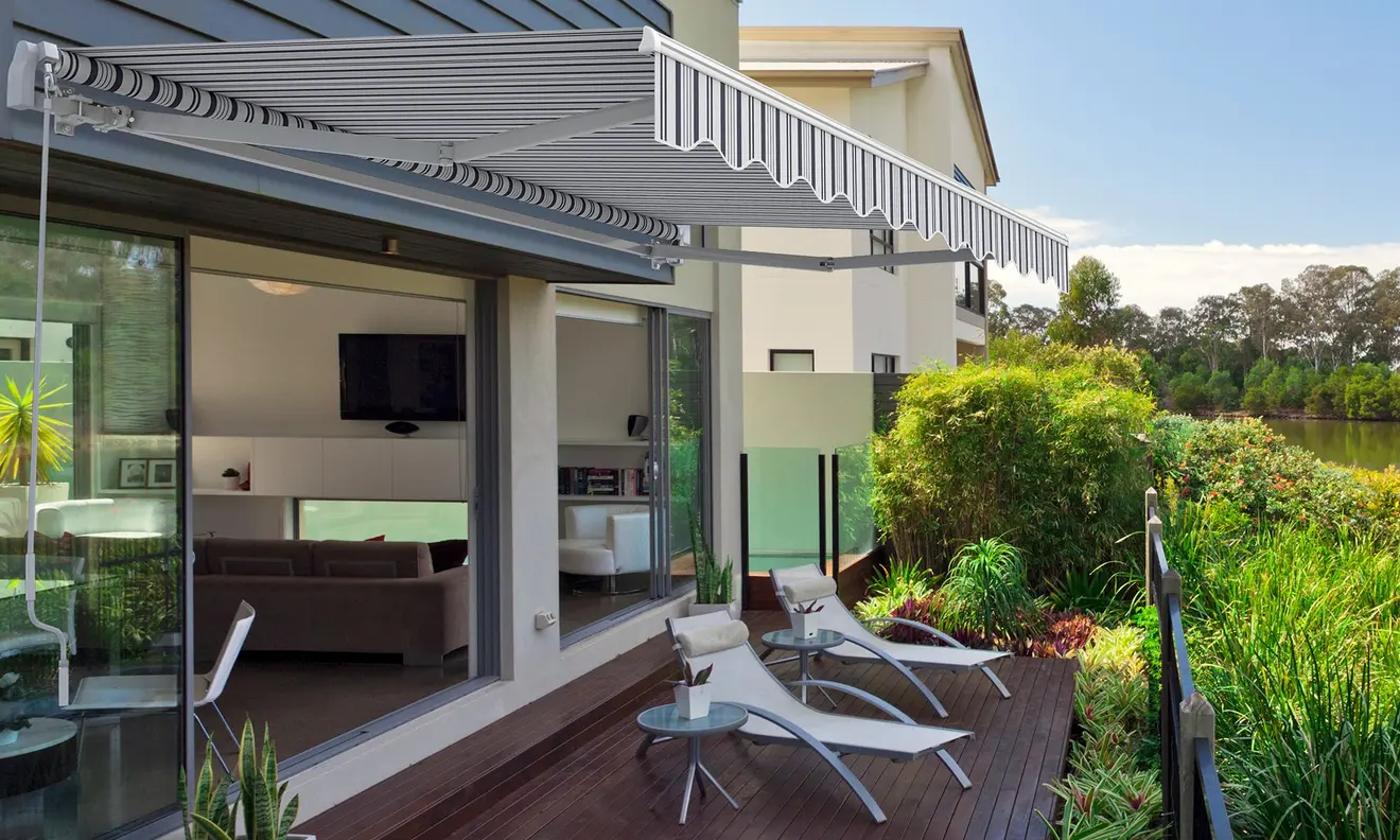 Gelenkarmmarkise Basic 2000 über Terrasse mit Liegestühlen und Pflanzen im Hintergrund