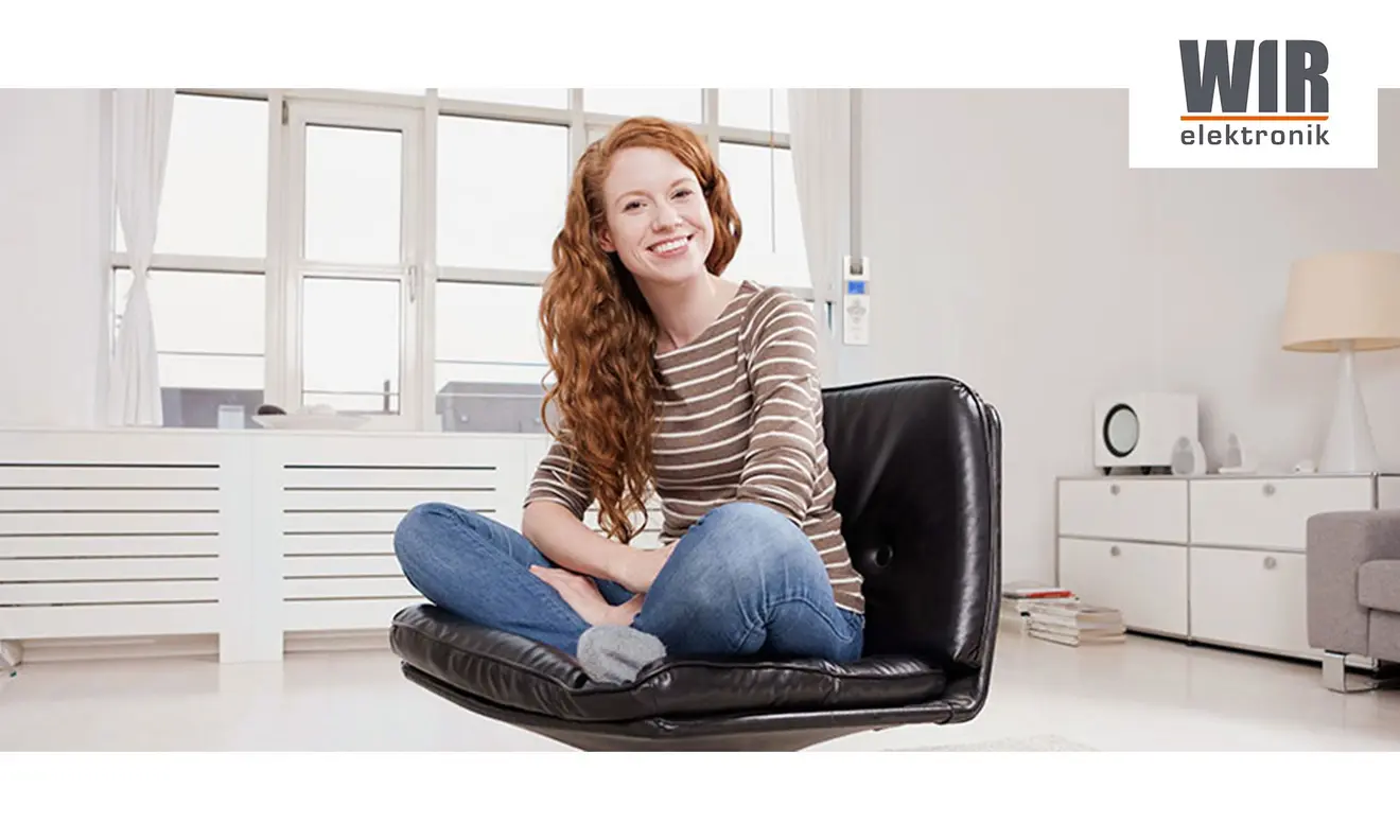 Eine Person sitzt auf einem Stuhl in einem modernen Wohnzimmer, im Hintergrund ein elektrischer Gurtwickler