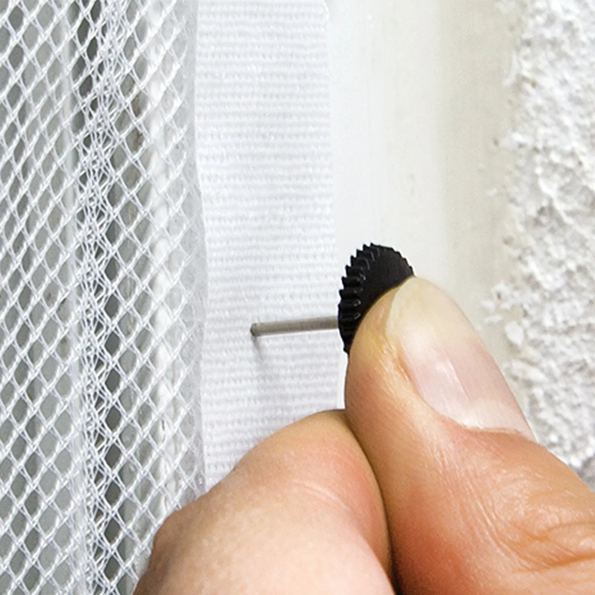 Mano che fissa un tessuto a rete con un piccolo chiodo a una superficie murale