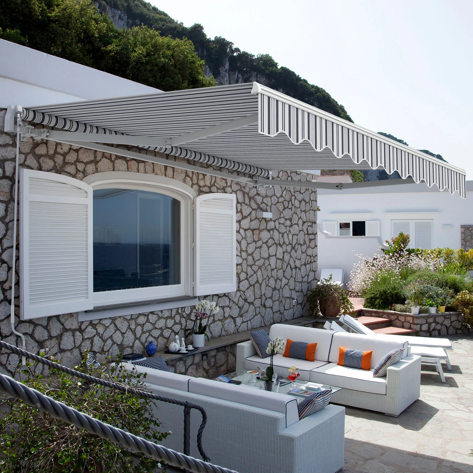 Tenda sopra la terrazza con area salotto e piante, montata su un muro di pietra di una casa