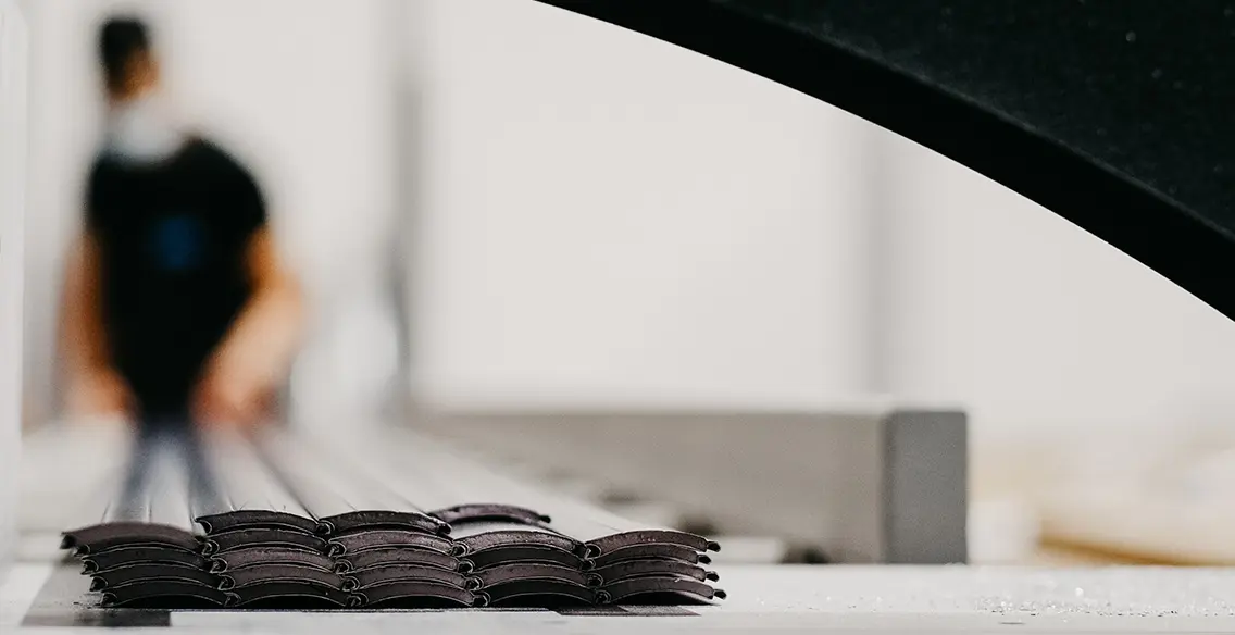 Stapel von gebogenen Metallteilen auf einem Tisch, unscharfe Person im Hintergrund