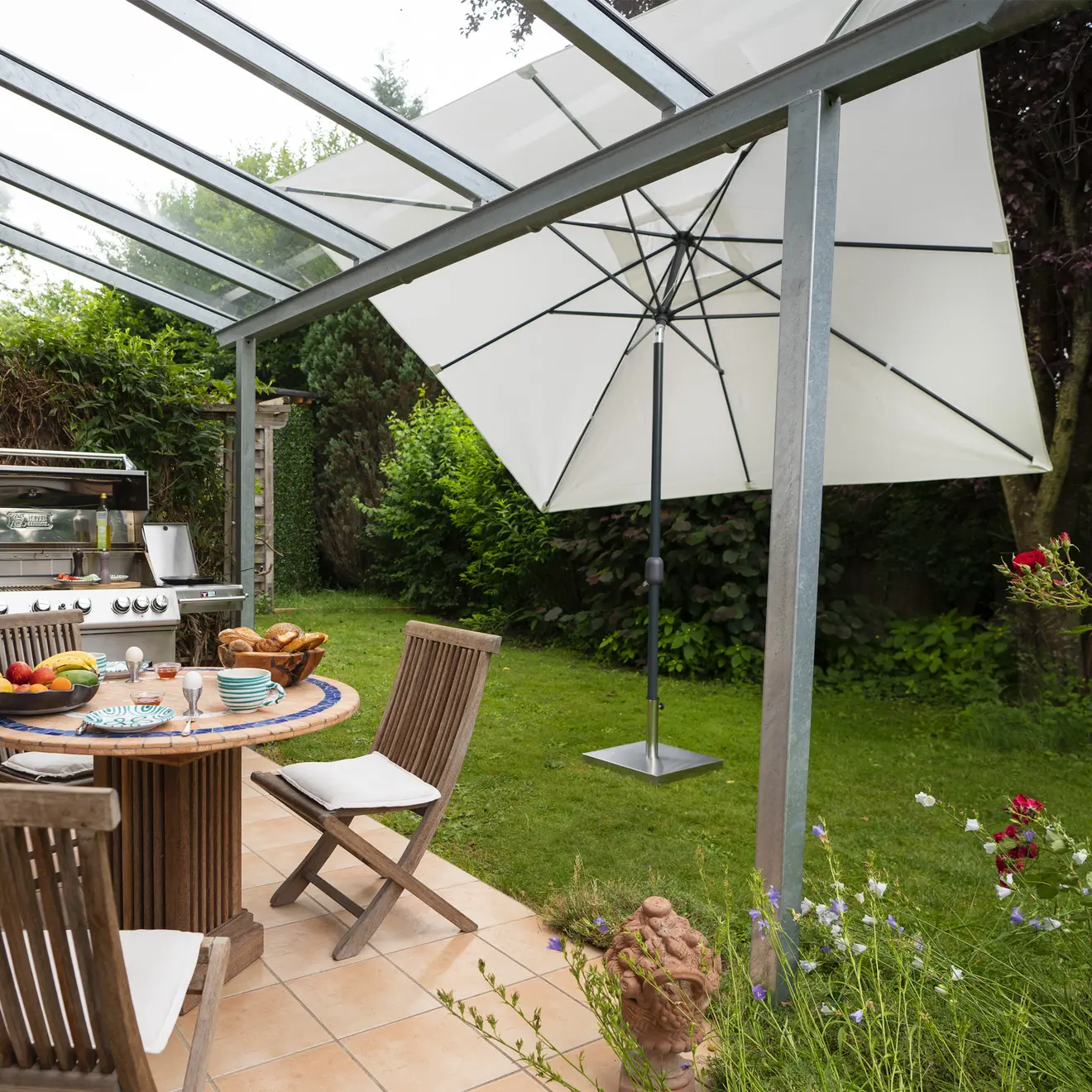 Sonnenschirm im Garten neben Terrasse mit Tisch, Grill und Holzstühlen