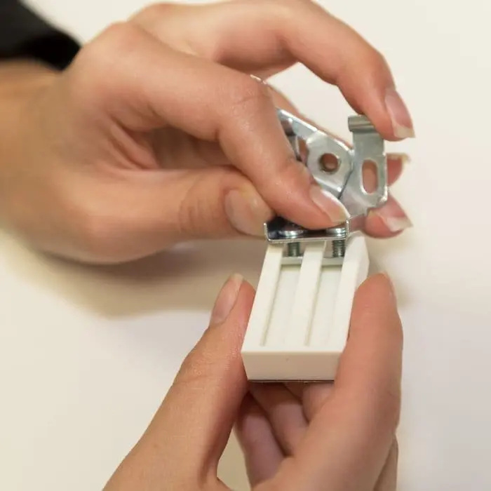 Hände halten einen Universal Haftträger mit Metallklammer, geeignet zur Befestigung von Gegenständen