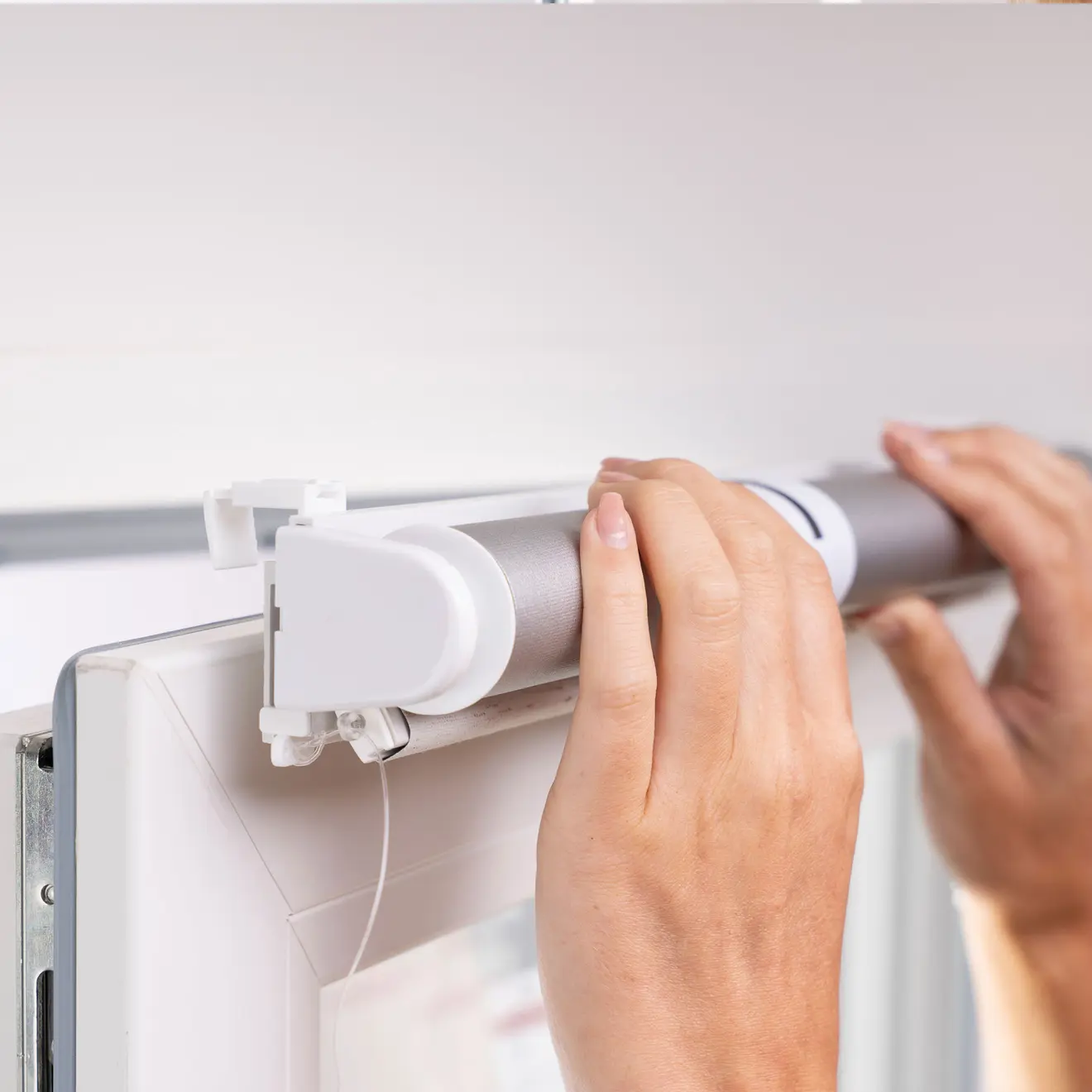 Manos instalando un estor enrollable sin taladrar en el marco de la ventana