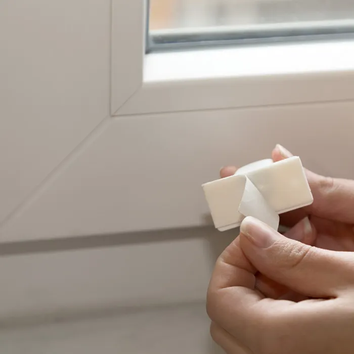 Due mani tengono un supporto magnetico per la parte inferiore delle persiane davanti a un telaio di finestra