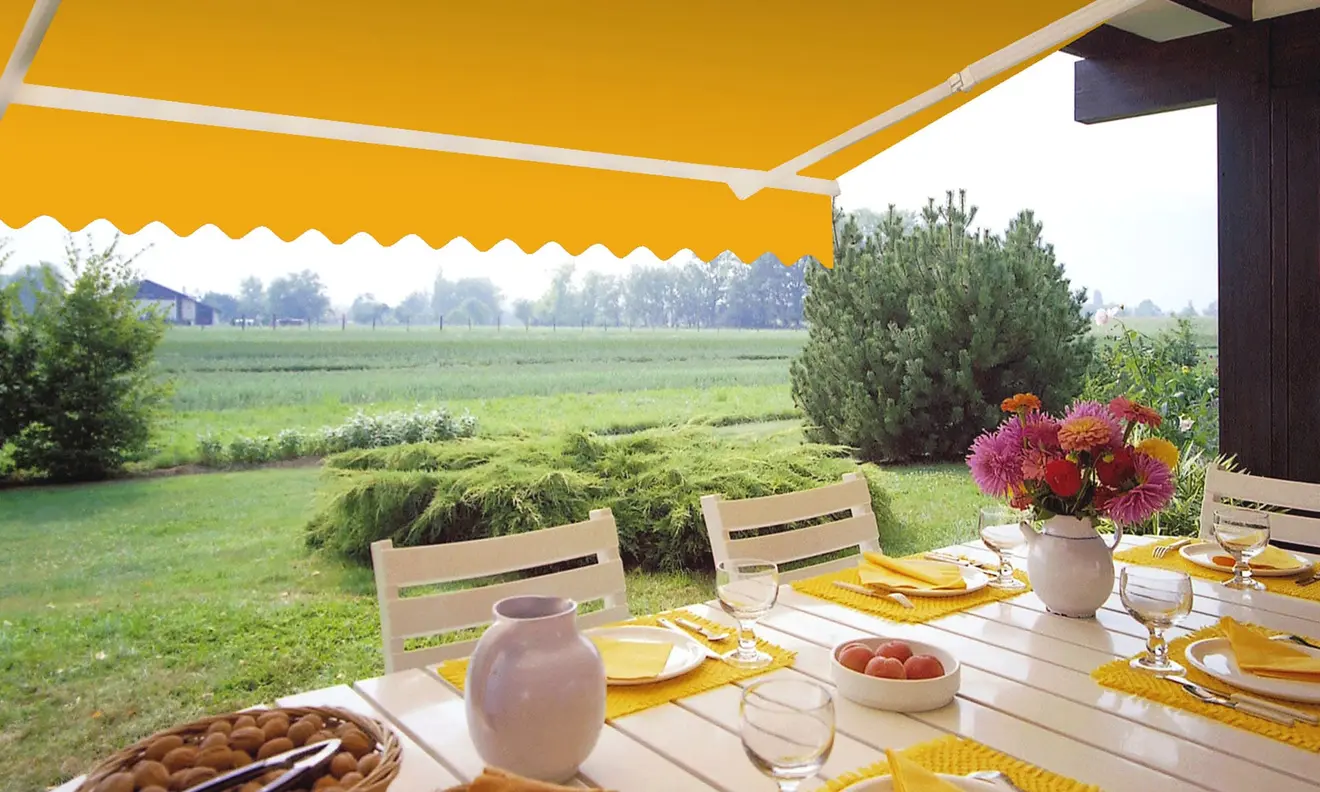 Gelenkarmmarkise Basic 2000 über einem gedeckten Gartentisch im Freien