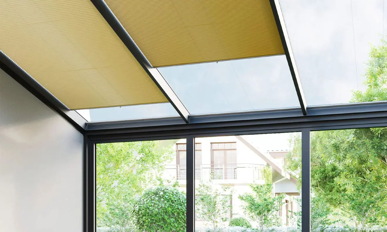 Ein Wintergarten mit Glasdach und integrierten Sonnenschutzplissees, umgeben von Bäumen und Sträuchern