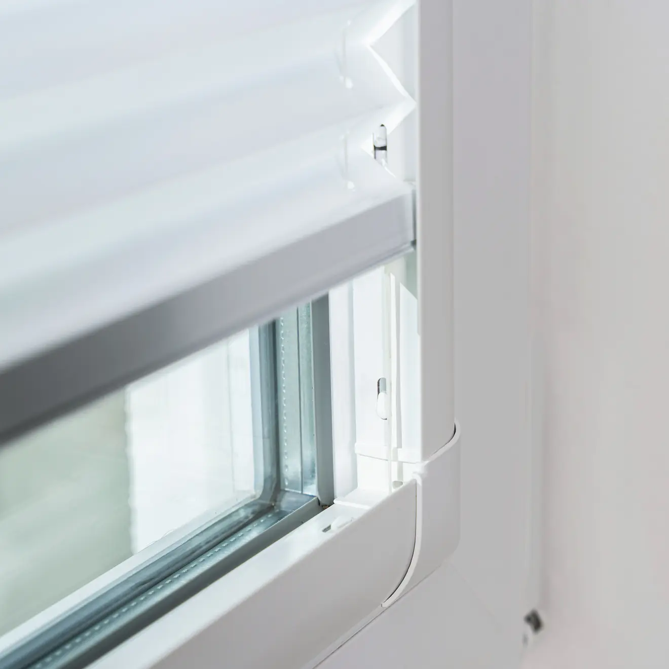 Detailansicht eines weißen Plissees mit Führungsschiene am Fensterrahmen