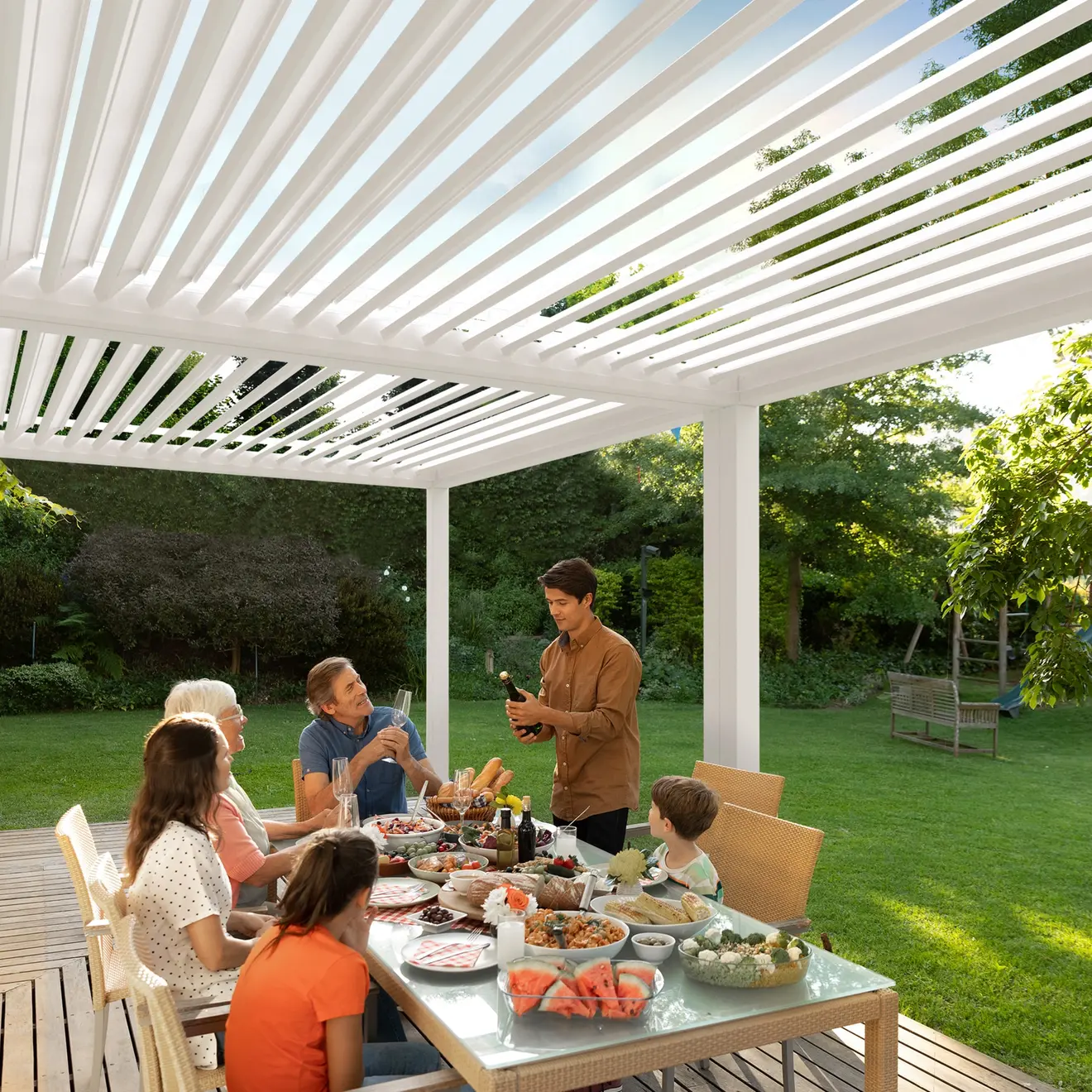 Menschen sitzen unter einer Pergola mit Lamellendach und essen an einem Tisch im Freien