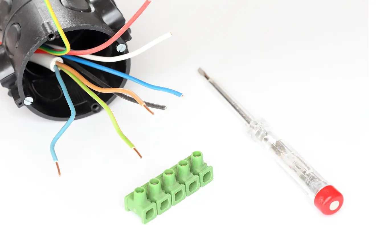 Unterputzdose mit Kabeln, Schraubendreher und Anschlussklemme auf weißem Hintergrund