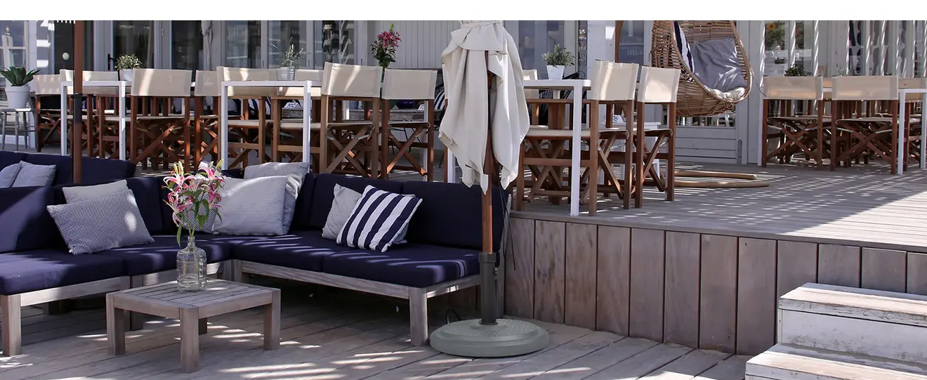 Sonnenschirm mit Schirmständer auf Terrasse neben Sitzbereich und Tischgruppe