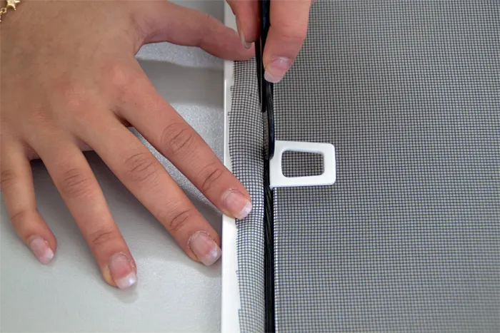 Mani usano lo strumento in PVC per fissare la protezione contro gli insetti nel telaio